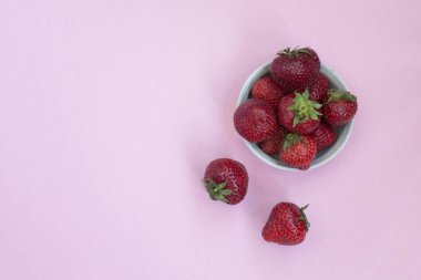 Bir tabak içinde Olgun kırmızı çilek. Pembe arka plan. Vitaminler ile gıdalar.