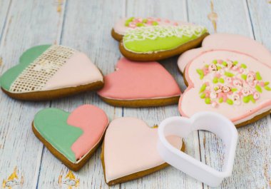 Pink and colored gingerbread and honey cakes and heart-shaped cookies lie in a messy pile on a light wooden background. Nearby are white molds for baking. Place for text. The concept of love, mother's clipart