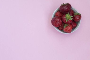 Bir tabak içinde Olgun kırmızı çilek. Pembe arka plan. Vitaminler ile gıdalar.