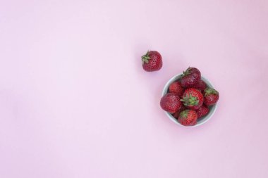 Bir tabak içinde Olgun kırmızı çilek. Pembe arka plan. Vitaminler ile gıdalar.