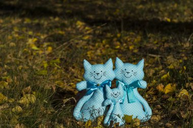 Three textile toys of a cat, sitting together on a yellow foliage, in a meadow. Family concept, child protection. Rummy background. clipart
