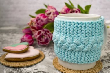 Pembe çiçekler lale ve tatlılar ile bir örme mavi durumda çay beyaz fincan, bir dokusal masada Gingerbread ile.