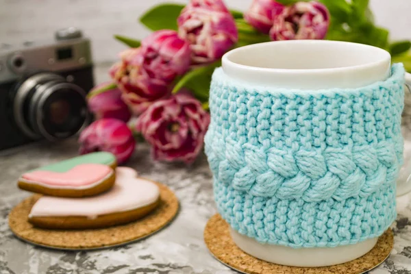 Una taza de té blanco en una caja azul de punto con una vieja cámara y flores rosas tulipanes y dulces, pan de jengibre en una mesa de textura . —  Fotos de Stock