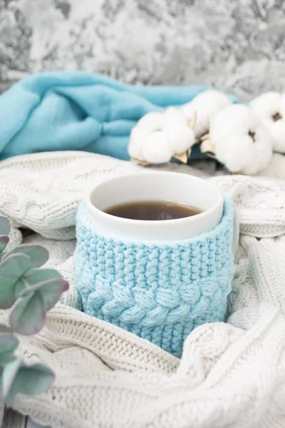 Taza blanca con té en un marco azul de punto y envuelto en un tejido a cuadros de punto blanco. En el fondo, ramitas de eucalipto y algodón. Desayuno en la cama. Acogedor . —  Fotos de Stock