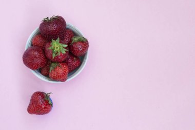 Bir tabak içinde Olgun kırmızı çilek. Pembe arka plan. Vitaminler ile gıdalar.
