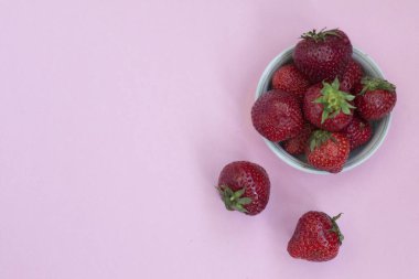 Bir tabak içinde Olgun kırmızı çilek. Pembe arka plan. Vitaminler ile gıdalar.