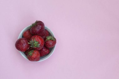 Bir tabak içinde Olgun kırmızı çilek. Pembe arka plan. Vitaminler ile gıdalar.