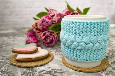 Pembe çiçekler lale ve tatlılar ile bir örme mavi durumda çay beyaz fincan, bir dokusal masada Gingerbread ile.