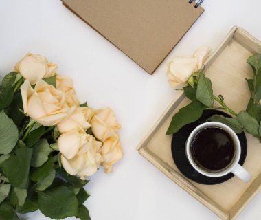 Gül bir buket ile şık düz kompozisyon, bir tabak üzerinde bir fincan çay ve beyaz ahşap bir tepsi. Satır zanaat levha yatıyor. Kadın iş mockup.