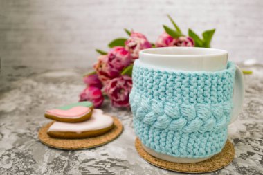 Pembe çiçekler lale ve tatlılar ile bir örme mavi durumda çay beyaz fincan, bir dokusal masada Gingerbread ile.