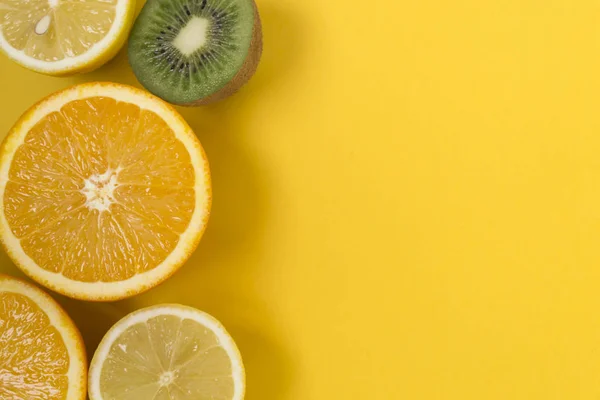 Marco de frutas exóticas sobre un fondo amarillo - limón, kiwi, naranja, vista superior . — Foto de Stock