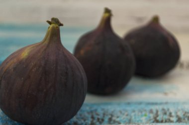Tahta beyaz bir masada üç taze incir. Üst üste düzenlenmiştir.