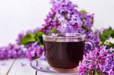 Ahşap beyaz arka planda leylak çiçekli bir fincan çay. Kartpostallar için Mocap. Bahar geldi. Leylaklı vazo. Uzayı metin için kopyala. Tatil kavramı ve günaydın dilekleri..