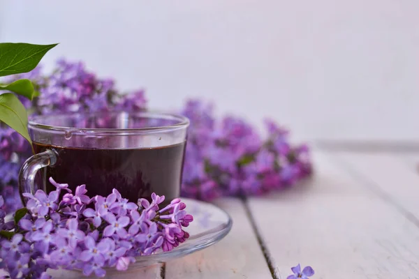 木の白い背景にライラックの花とお茶のカップ 郵便はがきのためのモカップ 春の時間だ ライラックと花瓶 テキストのスペースをコピーします 休日と朝の願いの概念 — ストック写真