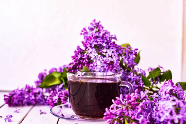Cup of tea with lilac flowers on a wooden white background. Mocap for postcards. Spring time. Vase with lilacs. Copy space for text. The concept of holidays and good morning wishes.