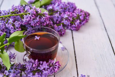 Ahşap beyaz arka planda leylak çiçekli bir fincan çay. Kartpostallar için Mocap. Bahar geldi. Leylaklı vazo. Uzayı metin için kopyala. Tatil kavramı ve günaydın dilekleri..