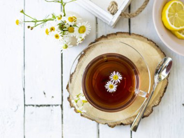 Bir fincan papatya çayı ve beyaz tahta üzerinde papatya çiçekleri olan bitki çayı. Yakınlarda bir vazo beyaz çiçek duruyor. Boşluğu kopyala