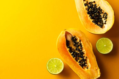 Sarı kesimli papaya ve yeşil limonlu sarı arka plan. Sınırlı, olgun tropik meyveler. Uzayı kopyala Sağlık kavramı.