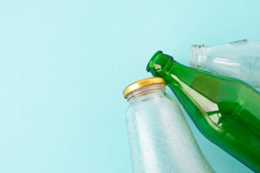 Boş bardaklar şeffaf ve mavi arka planda yeşil şişeler. Mekanın bir kopyası. Ekoloji ve Sıfır atık kavramı.