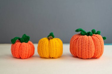 Gri bir zemin üzerinde turuncu ve sarı balkabağı dekoru örülmüş üç balkabağının sonbahar kompozisyonu, iplik ve dikiş, yumuşak ışık.