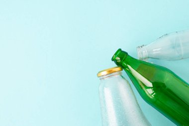 Boş bardaklar şeffaf ve mavi arka planda yeşil şişeler. Mekanın bir kopyası. Ekoloji ve Sıfır atık kavramı.