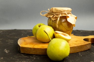 Cam kavanozda armut reçeli. Kavanoz el işi kağıdıyla kaplanmış ve jüt bir iple bağlanmış. Tatlı reçel kesme tahtasının üzerinde duruyor ve taze sarı armut meyveleri yakınlarda duruyor..