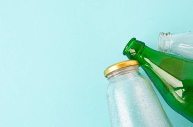 Boş bardaklar şeffaf ve mavi arka planda yeşil şişeler. Mekanın bir kopyası. Ekoloji ve Sıfır atık kavramı.