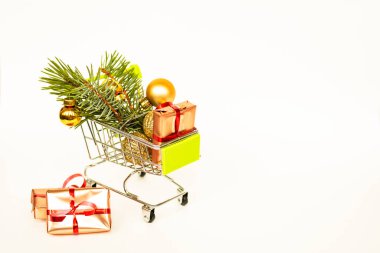 Altın hediye kutuları ve Noel baloları olan market sepeti, arka planda beyaz afişlerle süslenmiş Noel ağacı filizi. Xmas indirimi. İnternetten Noel alışverişi. Kış tatili indirimleri, mevsimlik satışlar, Kara Cuma, Noel, indirim.