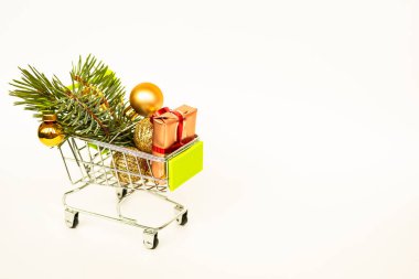 Altın hediye kutuları ve Noel baloları olan market sepeti, arka planda beyaz afişlerle süslenmiş Noel ağacı filizi. Xmas indirimi. İnternetten Noel alışverişi. Kış tatili indirimleri, mevsimlik satışlar, Kara Cuma, Noel, indirim.