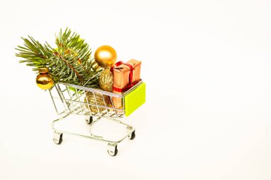 Altın hediye kutuları ve Noel baloları olan market sepeti, arka planda beyaz afişlerle süslenmiş Noel ağacı filizi. Xmas indirimi. İnternetten Noel alışverişi. Kış tatili indirimleri, mevsimlik satışlar, Kara Cuma, Noel, indirim.