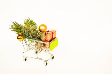 Altın hediye kutuları ve Noel baloları olan market sepeti, arka planda beyaz afişlerle süslenmiş Noel ağacı filizi. Xmas indirimi. İnternetten Noel alışverişi. Kış tatili indirimleri, mevsimlik satışlar, Kara Cuma, Noel, indirim.