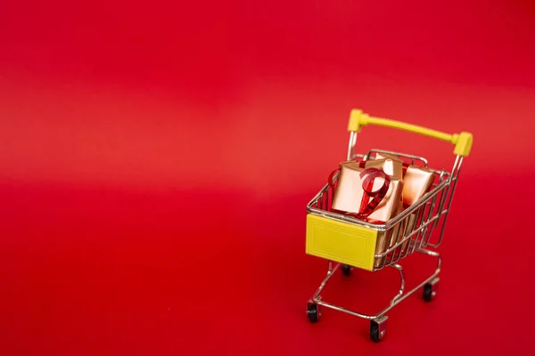 Xmas sale. Grocery basket with golden gift boxes with red ribbon on red background banner with copy space. Christmas shopping online. Winter holiday sales, seasonal sales, Black Friday, Christmas — Stock Photo, Image