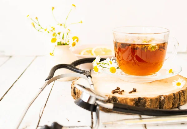 Decoction of chamomile, dried flower in flower tea and a phonendoscope, sliced lemon on a white wooden background. Health concept, prostate treatment, doctor prescribing treatment.