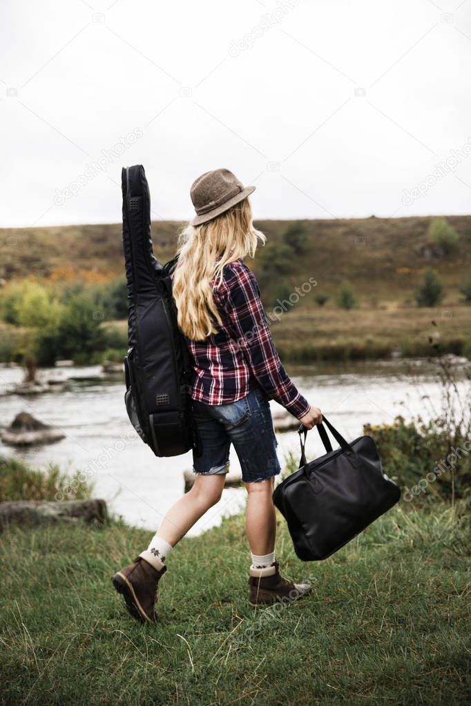 Girl travels with guitar and bags.Young Girl with a guitar and an old suitcase. Nature. Travel lifestyle. Teenager, young people.