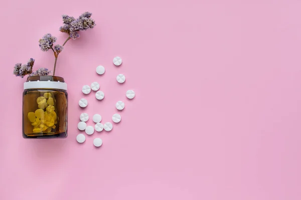 A bottle of medicines and scattered pills on a pastel pink background. Ripped vitamins on a bright background. healing herbs.