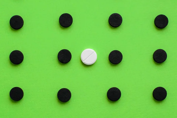 Koncepcionális orvosi háttér fekete kapszulák aktivált szénnel és fehér tablettával, zöld háttérrel. Felülnézet, másolási tér. — Stock Fotó
