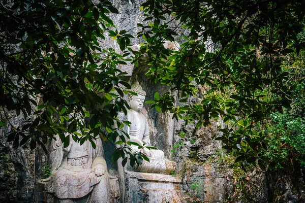 Ancient Buddhist statues carved in rocks hidden behind green leaves in Linying Temple of Hangzhou, China