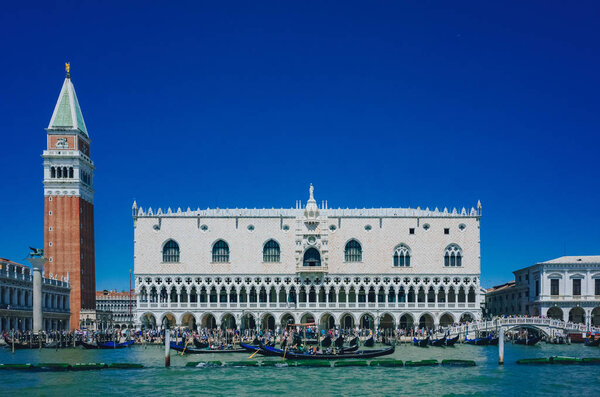 View of Ducal Palace, St. Mark's Bell Tower over water and gondolas, under blue sky, in Venice, Italy