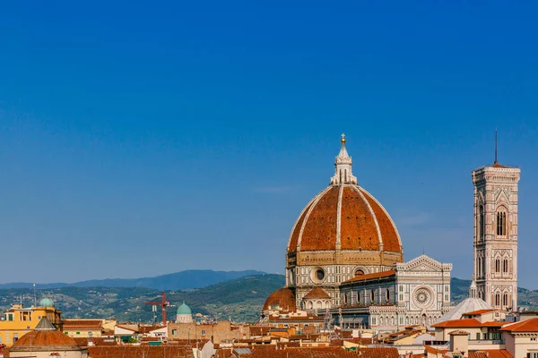 View of the Florence Cathedral and Giotto\'s Bell Tower under blue sky, over houses of the historical center of Florence, Italy