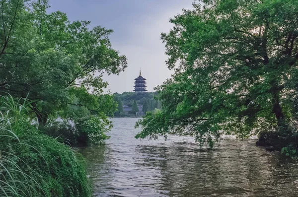 View of Leifeng Pagoda over hills and West Lake, between trees, in Hangzhou, China
