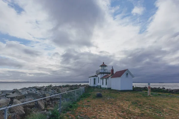 Victorian-era lighthouse under clouds by water in Discovery Park of Seattle, USA