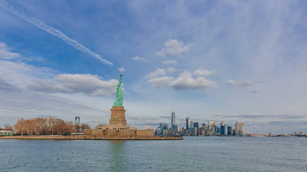 View of Statue of Liberty overlooking buildings of downtown Manhattan by water, in New York City, USA