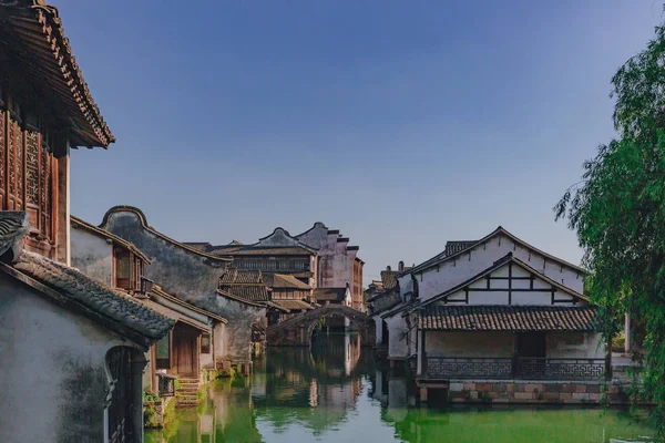 View of traditional Chinese houses and bridge by water under blue sky, in the old town of Wuzhen, China