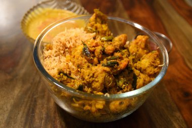 Hint Tavuğu Biryani, ahşap zemin üzerinde köri ve sosis bulunan cam bir kasede servis edilir.