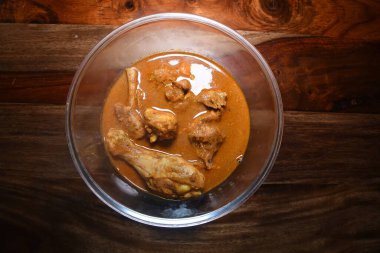 Ahşap arka planda şeffaf bir kasede servis edilen körili tavuk.