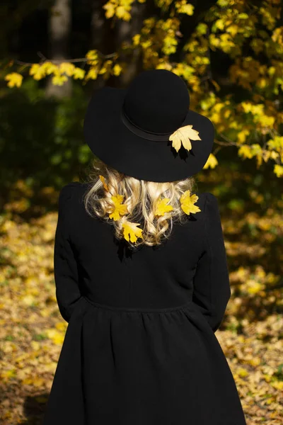 Yellow maple leaves. The girl in the hat and the yellow leaves of the maple. Autumn and yellow leaves of maple.
