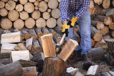 Endüstriyel balta tutan adam. Balta elinde. Güçlü bir adam elinde testereler ve yakacak odunların arka planına karşı bir balta tutar. Elinde balta olan güçlü bir oduncu. Elektrikli testereyi kapat..