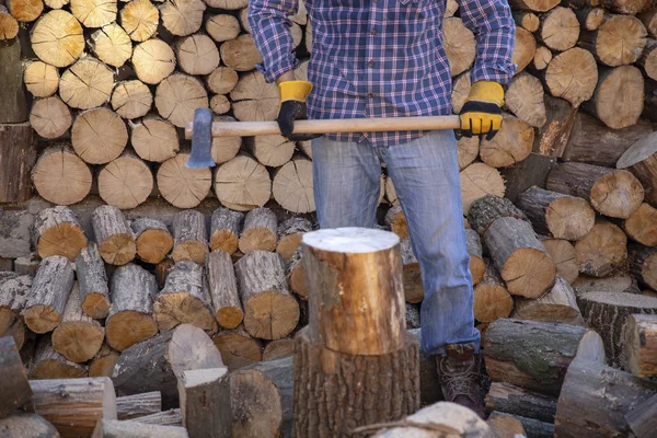 Un homme tenant une hache industrielle. Ax à la main. Un homme fort tient une hache dans ses mains sur fond de tronçonneuses et de bois de chauffage. Homme fort bûcheron avec une hache à la main. tronçonneuse gros plan. — Photo