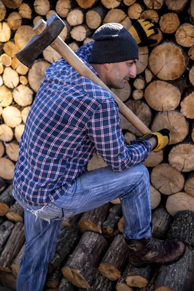 Un uomo con un'ascia industriale. Ax in mano. Un uomo forte tiene in mano un'ascia sullo sfondo di motoseghe e legna da ardere. Uomo forte boscaiolo con un'ascia in mano. motosega da vicino. — Foto Stock