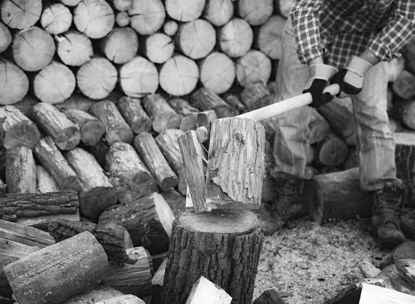 Een man met een industriële bijl. Ax in de hand. Een sterke man houdt een bijl in zijn handen tegen de achtergrond van kettingzagen en brandhout. Sterke houthakker met een bijl in zijn hand. Kettingzaag van dichtbij. — Stockfoto